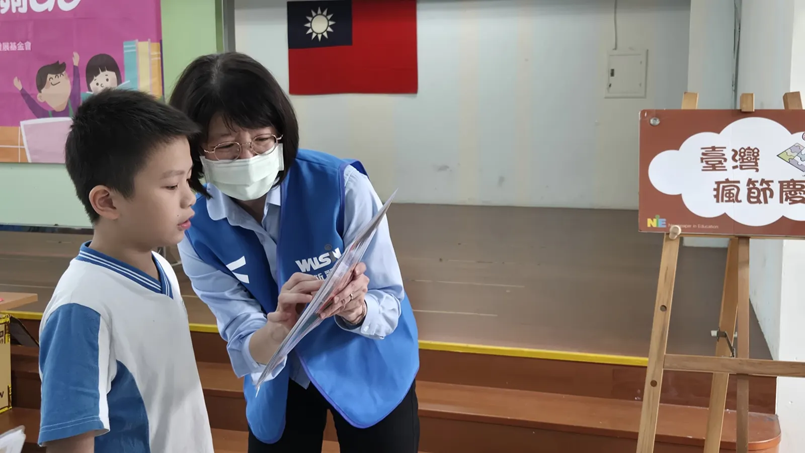 志工彎腰陪學童看題卡,閱讀教育推廣活動